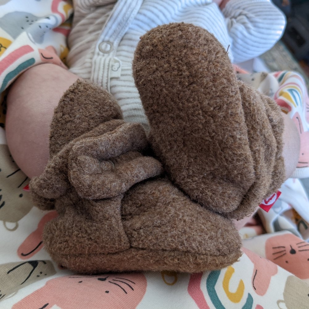 Close up of a newborn's legs with Zutano fleece booties on, the best soft sole barefoot booties for babies and toddlers