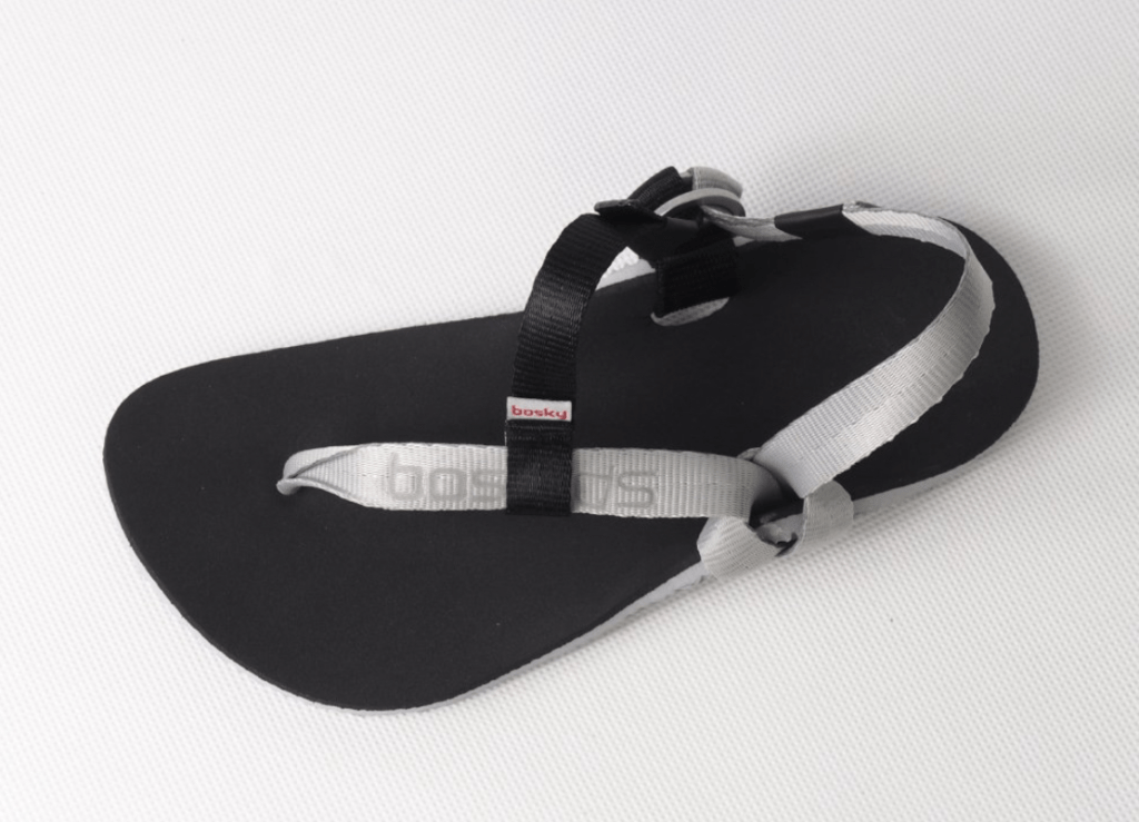 A pair of black barefoot kids sandals with rubber soles and tough black and silver straps on a white background