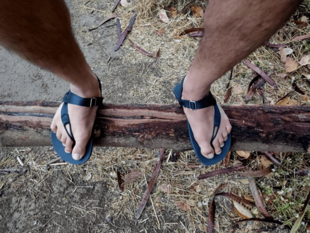 A pair of black adventure barefoot sandals shown atop a log in the woods