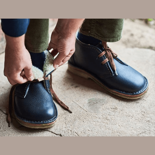 A pair of blue leather wide toe box boots being put on, close up of a man's hand securing the boots