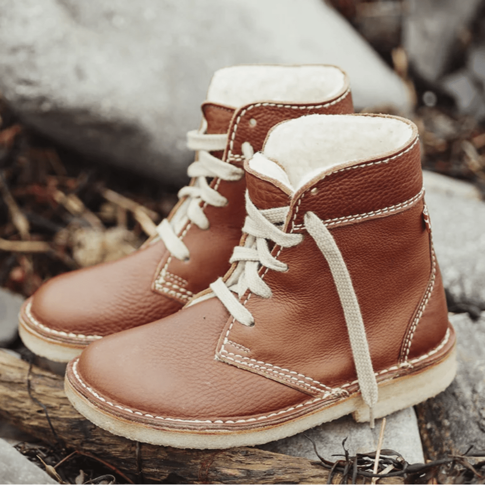 A pair of brown leather duckfeet boots sitting unworn outside on rocks, they have a conventional heeled sole, without interior support, and a wide toe box