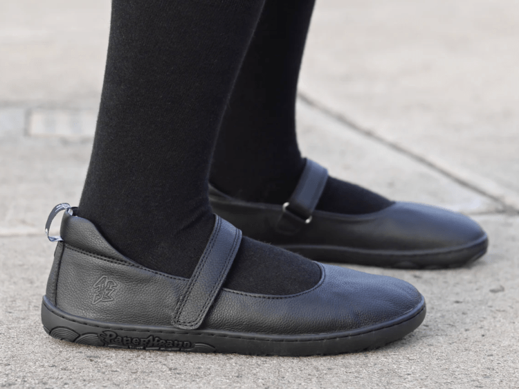 Side view of a young girl in black tights and PaperKrane black leather barefoot mary janes with a wide toe box