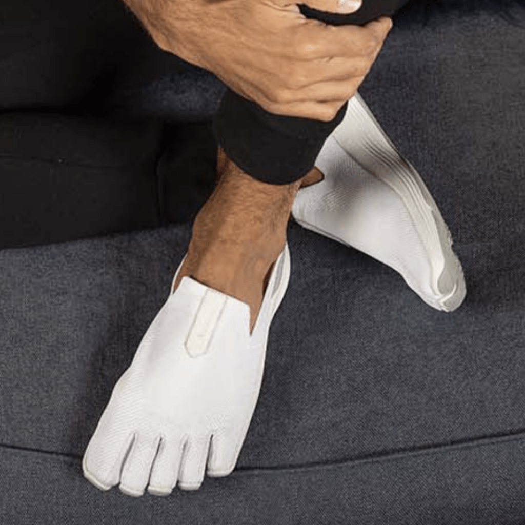 A pair of men's feet wearing slip on white sneakers with 5 toe pockets for foot function