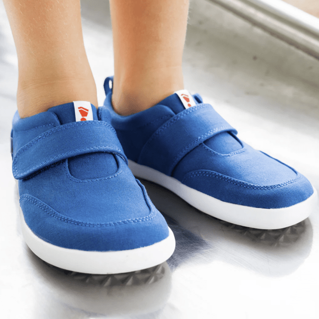 A young child wearing blue canvas Splay Explore 2.0 barefoot flexible velcro everyday sneakers