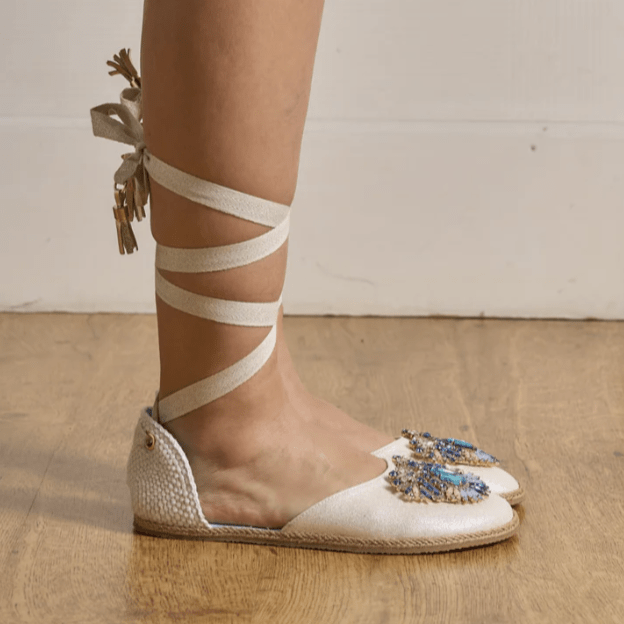 A pair of embellished Espadrilles that are lace up the leg and tied in the back. Vega Barefoot fancy espadrilles with a wide toe box being worn by a person standing with their feet together and pointed to the right.